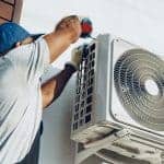 Repairman in uniform installing the outside unit of air conditioner
